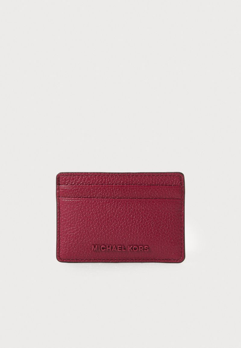 Burgundių atspalvio kortelių laikiklis su tekstūruota oda, turintis kelis skyrius ir iškilnią "MICHAEL KORS" logotipą priekyje.