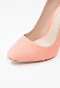 Chaussure à talon haut en daim rose avec un bout pointu et une doublure intérieure lisse, présentant une silhouette élégante et un design effilé.