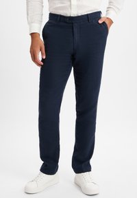 Marineblaue Leinenhose mit geradem Schnitt, ausgestattet mit einem Knopfverschluss, Seitentaschen und einer glatten Textur, kombiniert mit weißen Sneakers.