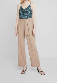 Leopardprint cami in teal en zwart gecombineerd met beige high-waisted broek met een strik in de taille. Zwarte enkelbandjes hakken.