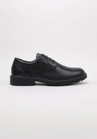 Chaussure de ville pour homme en cuir noir, à lacets, avec un petit talon et une semelle robuste, vue de côté sur un fond uni.
