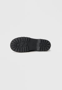 Black rubber boot sole featuring deep treads and star patterns for traction, with a smooth texture and a sturdy, flat design.