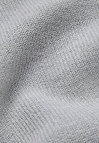 Jasnoszara dzianina o fakturze prążkowanej, ukazująca miękkie włókna i gładkie wykończenie.