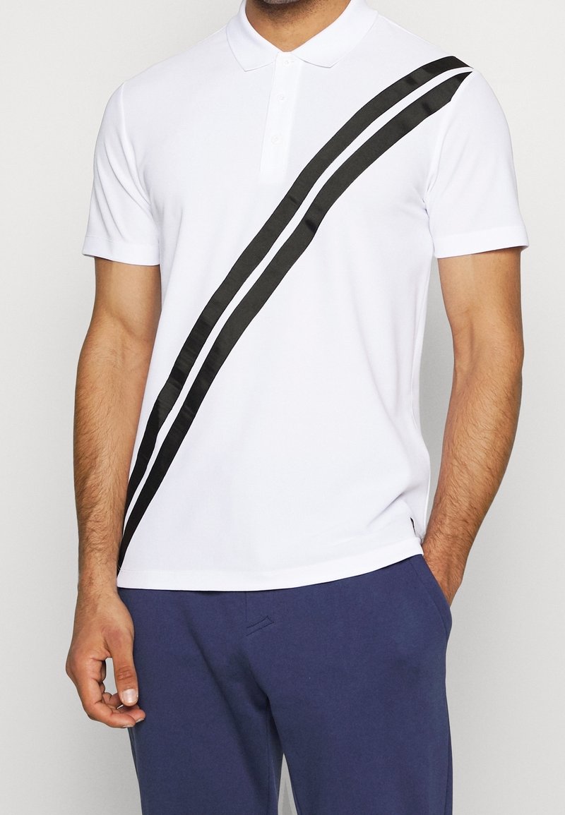 Bílá polo košile s diagonálním černým pruhem, krátké rukávy a klasický límec. Vyrobena z hladkého, lehkého materiálu.