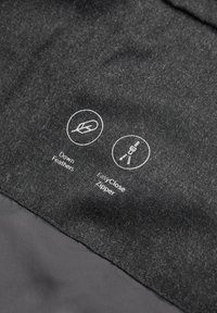 Fabric label showing icons and text indicating down feathers filling and an easy-close zipper on dark textile material.