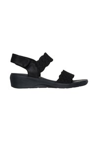 Sandalias de cuña negra con correas de tela trenzada, parte superior texturizada y una suela acolchada para mayor comodidad y soporte. Correa de tobillo ajustable.