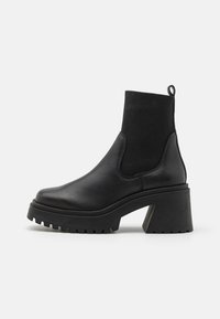 Musta nilkkurit, joissa on sileä nahkapäällinen, joustavat sivuosat, paksu tukkikorko ja kuvioitu kumipohja.