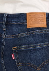 Dunkelblaue Jeans aus Denim mit einem Lederpatch auf der Rückseite, das mit "Levi Strauss & Co." beschriftet ist, und einem roten "Levi's"-Tag, ausgestattet mit klassischen Nähmustern.