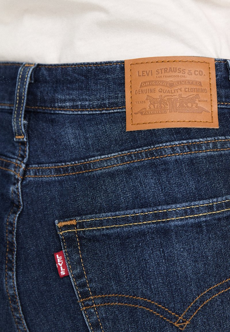 Dunkelblaue Jeans aus Denim mit einem Lederpatch auf der Rückseite, das mit "Levi Strauss & Co." beschriftet ist, und einem roten "Levi's"-Tag, ausgestattet mit klassischen Nähmustern.