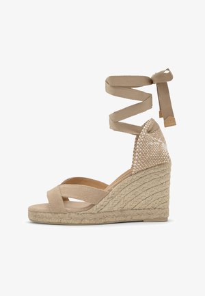 Beige woven wedge sandal with ankle wrap ties, braided jute platform, and open-toe crisscross straps.