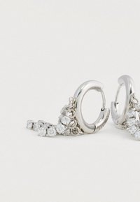 Ασημένια σκουλαρίκια δαχτυλίδι με κρεμασμένα μικρά τετράγωνα διαυγή πετράδια σε ανοιχτό φόντο.