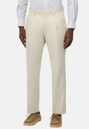Pantalons en coton beige à coupe droite, avec des plis à l'avant. Portés avec une chemise à col bleu clair et des chaussures couleur miel.