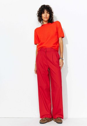Pantalons rouges amples avec des plis, associés à un haut orange à manches courtes. La tenue comprend des chaussures à imprimé animal.