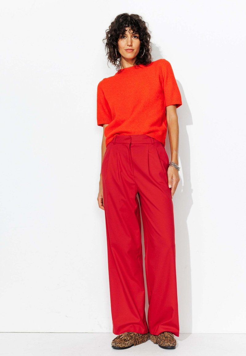 Pantalons rouges amples avec des plis, associés à un haut orange à manches courtes. La tenue comprend des chaussures à imprimé animal.
