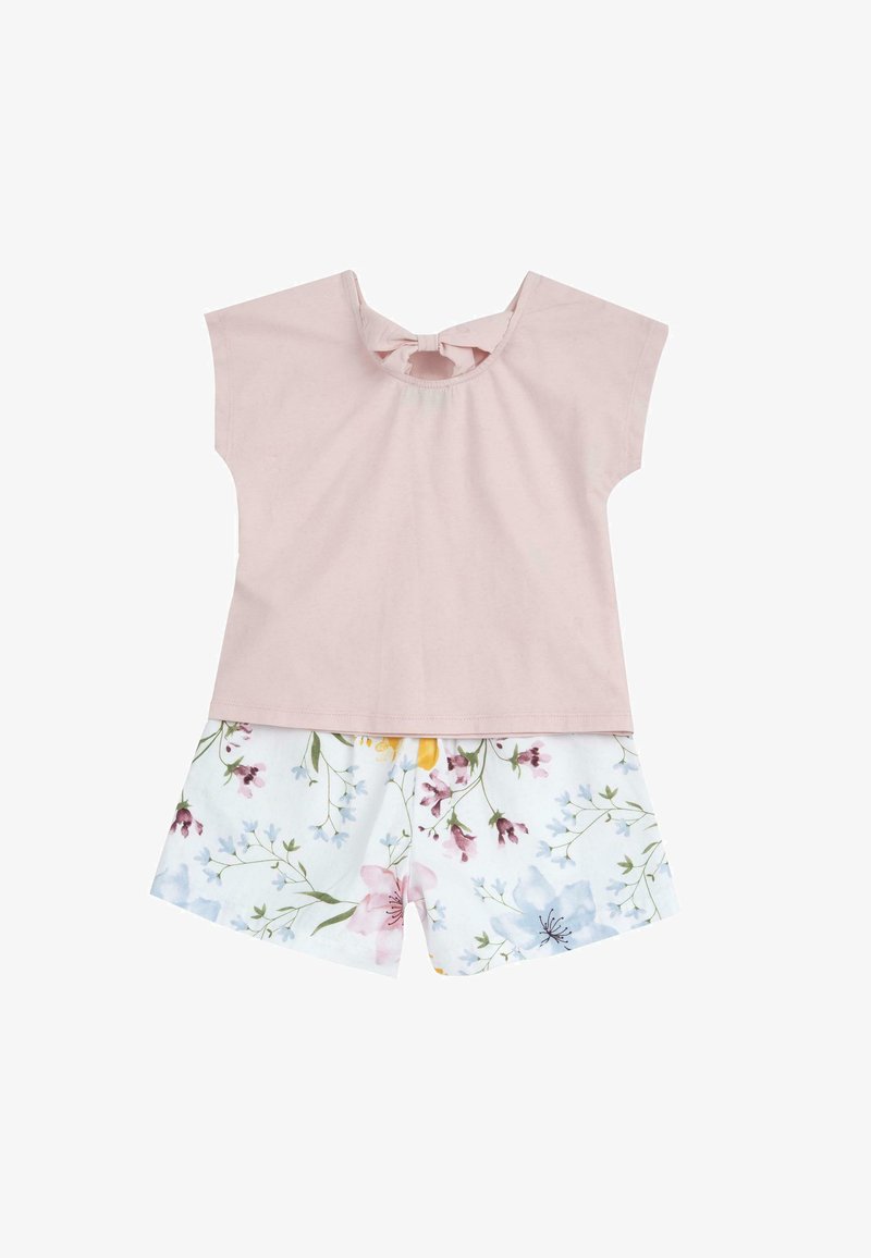 Lyserød bomuldsbluse med korte ærmer og sløjfe på ryggen, parret med hvide shorts med et farverigt blomstermønster og grønne accenter.