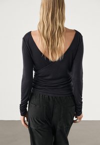 Czarny top z długim rękawem i dekoltem w kształcie litery V z tyłu, o dopasowanym kroju i marszczeniami w talii, zestawiony z luźnymi czarnymi spodniami z tylnymi kieszeniami.