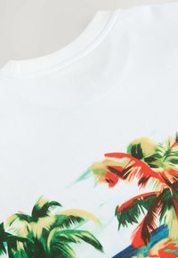 Hvid T-shirt med et farverigt palmetræ tryk. Har livlige grønne og røde farver, blødt bomuldsstof og et klassisk rundhalsdesign.
