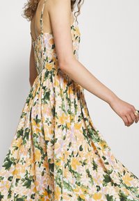 Vestido midi floral en amarillo, verde y rosa, con tirantes ajustables, cuerpo entallado, espalda fruncida y falda fluida con pliegues.