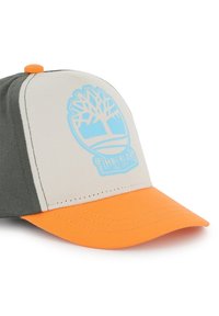 Casquette de baseball avec un corps en tissu gris et beige, une visière orange et un logo Timberland bleu avec un design d'arbre à l'avant.