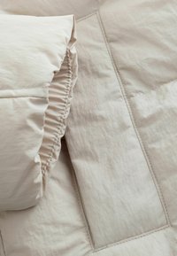 Lys beige quiltet tæppe med en struktureret overflade. Puffet kant samlet med elastik, med synlige detaljer og glatte sømme.