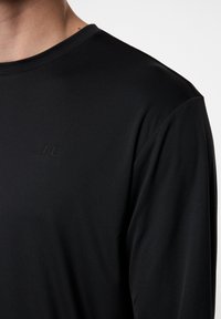 Mustapaita pitkillä hihoilla, valmistettu sileästä kankaasta. Ominaisuuksiin kuuluu pyöreä kaula-aukko ja huomaamaton logo rinnassa. Slim fit -malli, jossa on minimaalisesti saumoja.