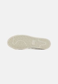 Shoe sole in off-white rubber with a wave pattern for traction. Smooth texture with subtle branding. Rounded edges and flexible design.