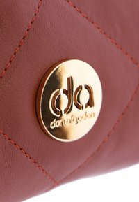Bolso de mano de cuero rojo con patrón de rombos acolchados, que presenta un logo circular dorado y costuras naranjas en contraste para un detalle adicional.