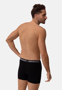 Zwarte katoenen boxer briefs met een contrasterende elastische tailleband waarop "ENDURANCE" staat. Het model wordt van achteren bekeken, wat de aansluitende stijl laat zien.