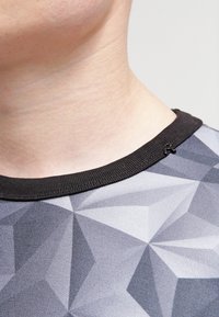 T-shirt graphique présentant un motif géométrique gris, un col côtelé noir, un tissu doux et des coutures plates pour un ajustement confortable.