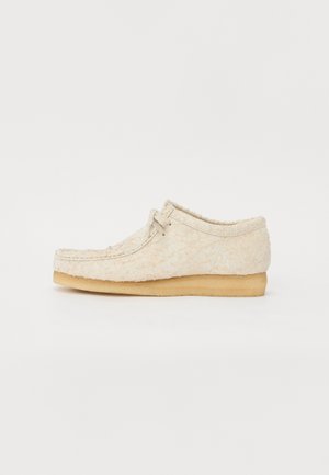 Beige suede shoe with a textured finish, lace-up design, and a light brown rubber sole. Rounded toe and minimalistic style.