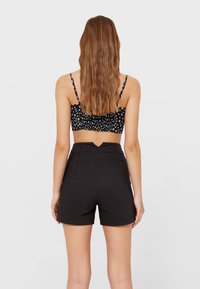 Zwarte short met hoge taille, een gladde textuur, plooien aan de voorkant en een v-vormig detail aan de achterkant. Gecombineerd met een zwarte cropped top met bloemenmotief.