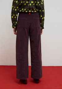 Pantalon à jambes larges de couleur violet foncé avec un tissu texturé. Comprend deux poches arrière et un accent rouge sur la ceinture.