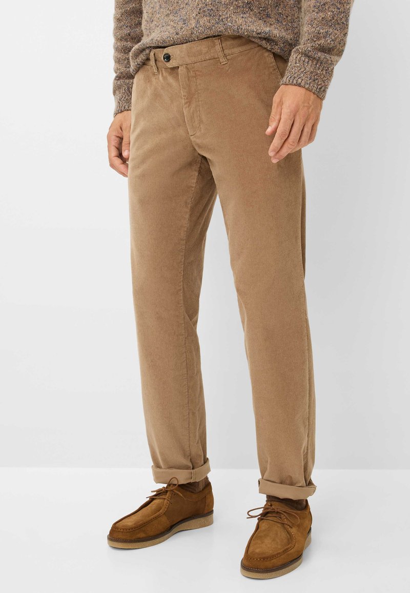 Bruine corduroy broek met een rechte pasvorm, voorzien van een knoopsluiting, riemlussen en opgerolde manchetten, gecombineerd met bruin suède schoenen.