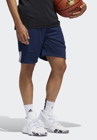 Marineblaue Basketballshorts mit drei weißen Streifen, kombiniert mit weißen Sneakers, die eine schwarz-weiße marmorierte Sohle und strukturierte Akzente haben.