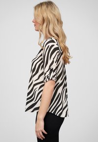 Loose-fitting, short-sleeve blouse in a black and white zebra print. Made of smooth fabric, featuring rolled sleeves and a rounded hem.