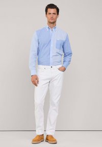 Camicia a maniche lunghe con righe blu e bianche, abbinata a pantaloni bianchi e scarpe slip-on marroni. Tessuto liscio, vestibilità sartoriale.
