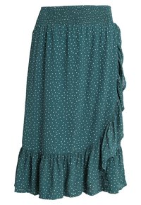 Tearskjorta med vita prickar. Har en smockad midja och en volangkant. Lättviktsmaterial med draperingsdetalj på ena sidan.