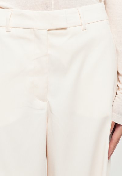 Pantaloni su misura color crema con frontale piatto, tasche laterali e una trama di tessuto liscia e leggera. Presentano passanti per cintura in vita.