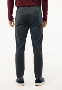 Ciemnoszare spodnie o prostym fasonie, z dwiema tylnymi kieszeniami zapinanymi na guziki oraz zwężającymi się nogawkami, zestawione z granatowymi trampkami.