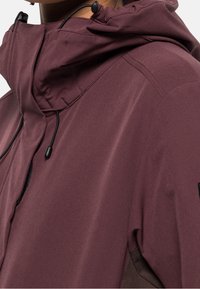 Veste bordeaux dotée d'un col montant, d'une capuche avec cordon de serrage et d'une finition noire. Texture lisse avec détail de poche latérale visible.