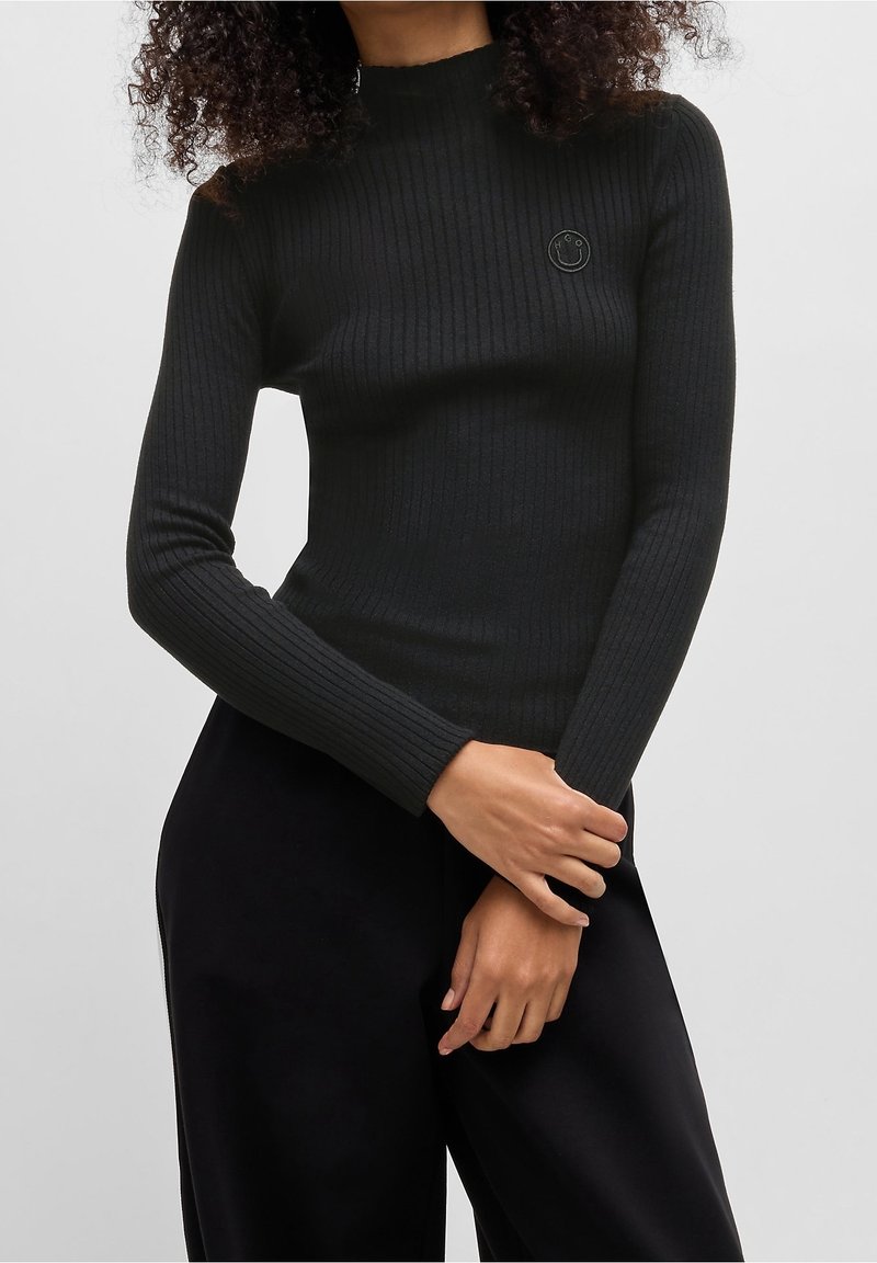 Schwarzes, geripptes Langarmoberteil mit hohem Halsausschnitt und kleinem gesticktem Smiley-Logo auf der Brust. Hat eine figurbetonte Silhouette und texturierten Stoff.