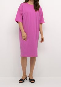 Fuksia suuruse T-särk-kleit lühikeste varrukatega, pehmest kangast; koos mustade punutud rihmaga kontsakingadega.