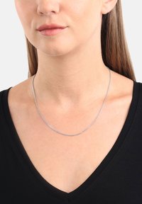 Silverfärgad kedjehalsband med en slät, tunn design, som vilar på en svart V-ringad topp och framhäver dess eleganta, metalliska textur.