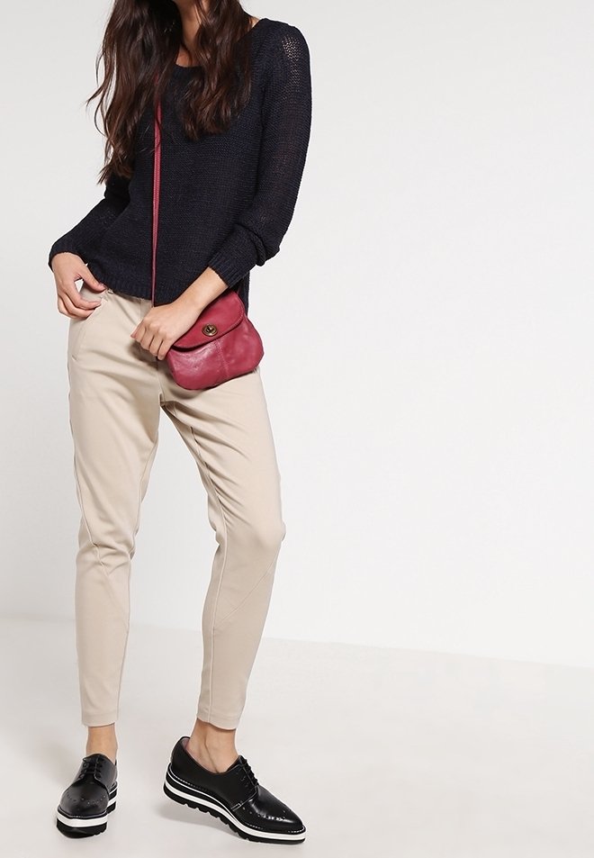 Marinblå stickad tröja, beige avsmalnande byxor och svarta snörskor. En liten röd väska över axeln ger en färgklick.