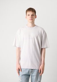 Kortærmet, lysegrå t-shirt i blødt stof, med en let oversized pasform og et diskret præget logo i midten.