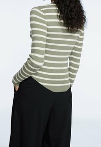 Groen- en witgestreepte ribbandtop met een aansluitend ontwerp, voorzien van lange mouwen en een ronde zoom, gecombineerd met zwarte broek.