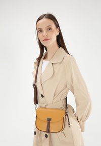 Braune und gelbe Umhängetasche aus strukturiertem Leder mit Klappenverschluss, ausgestattet mit einem braunen Tragegurt und silbernen Hardware-Akzenten.