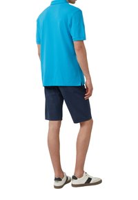 Turkusowa koszulka polo, krótki rękaw, prosta forma z bocznymi rozcięciami, zestawiona z granatowymi szortami. Białe sneakersy z czarnymi akcentami.