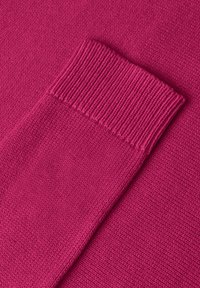 Gros plan d'une manche de pull en maille magenta pliée montrant une texture fine et un détail de bord-côte.