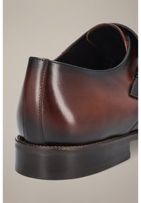 Brązowy, wypolerowany skórzany but z okrągłym obcasem, gładką teksturą i widocznymi detalami szycia. Klasyczny design i solidna podeszwa.